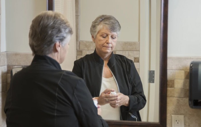 A woman with short hair looks at her reflection in a mirror while holding an object.