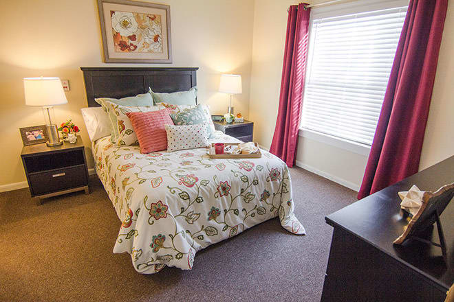 A cozy bedroom with a floral bedspread, pink curtains, and a bedside lamp.