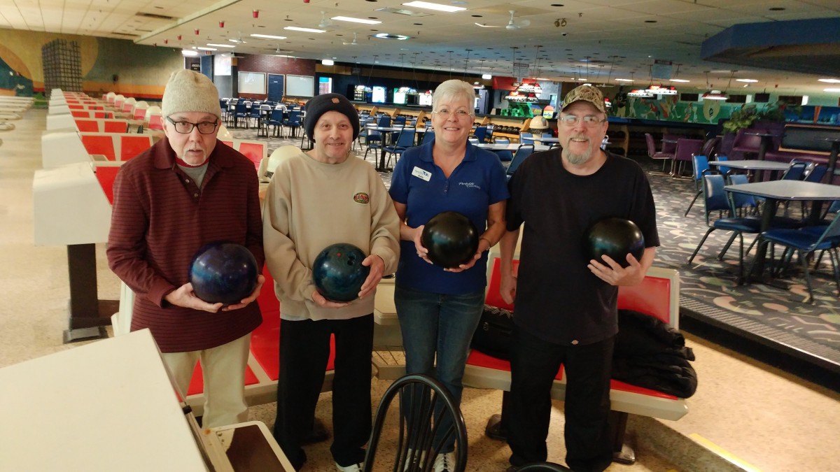 A group of four people holding bowling balls at a bowling alley.