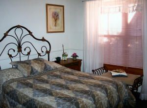 A cozy bedroom featuring a metal-framed bed, patterned bedding, and a softly lit window with curtains.