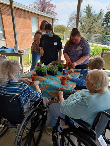 Seniors and caregivers enjoying a gardening activity, potting plants together in a sunny outdoor setting.
