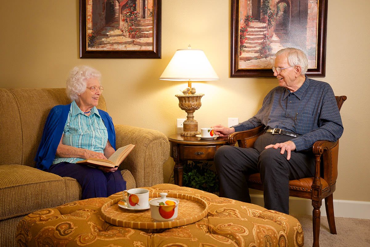 An elderly couple enjoying a cozy moment together in their living room, with tea and books.