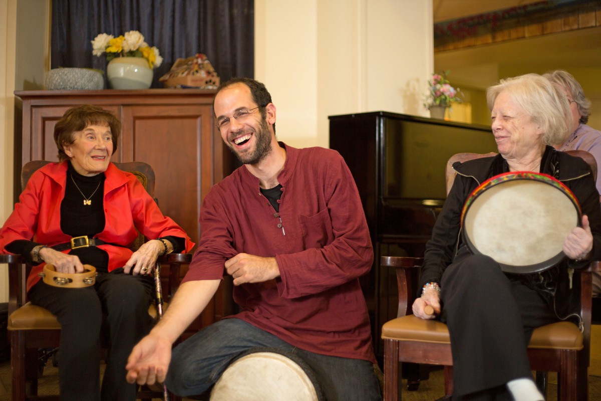 A group of people sitting indoors, laughing and engaged in conversation with a drum.