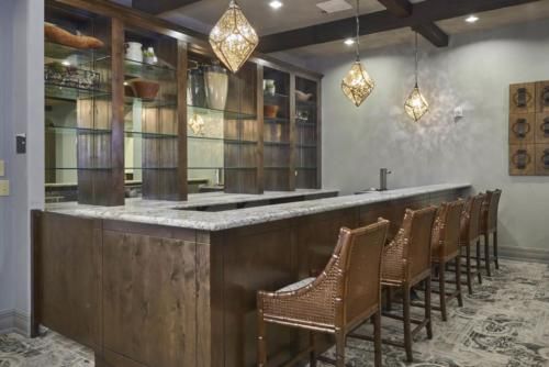 A stylish bar interior featuring a wooden countertop, leather chairs, and decorative pendant lights.