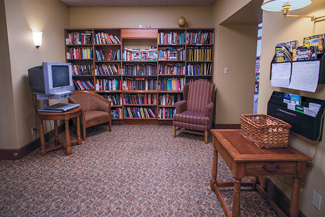 A cozy reading room with bookshelves, chairs, and a television.