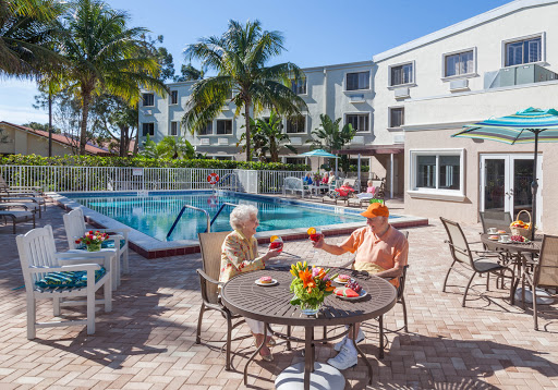 Two seniors enjoy a sunny day by the pool, savoring refreshments and good company.