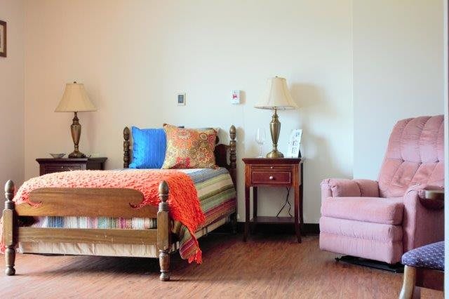 A cozy bedroom with a single bed, colorful pillows, and a side table with lamps.