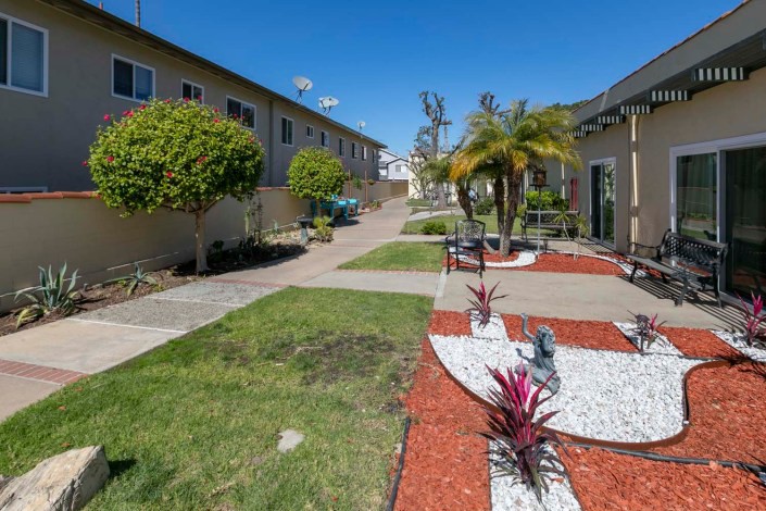 A well-maintained apartment courtyard featuring a landscaped garden with palm trees, pathways, and neatly trimmed lawns.