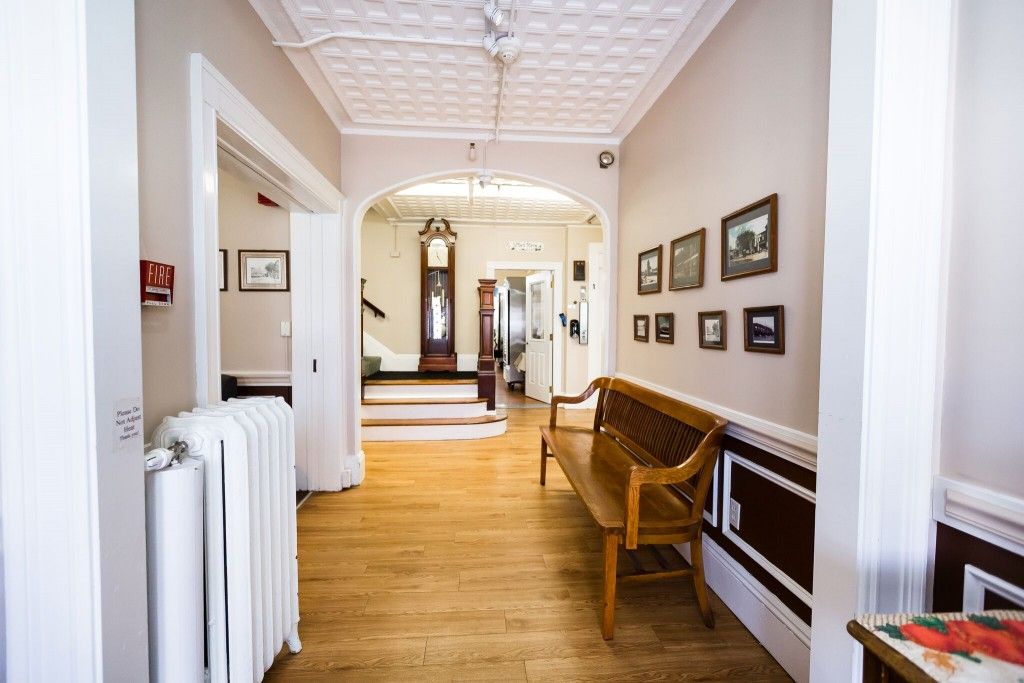A bright hallway with wooden floors, featuring antique furniture and framed pictures on the wall.