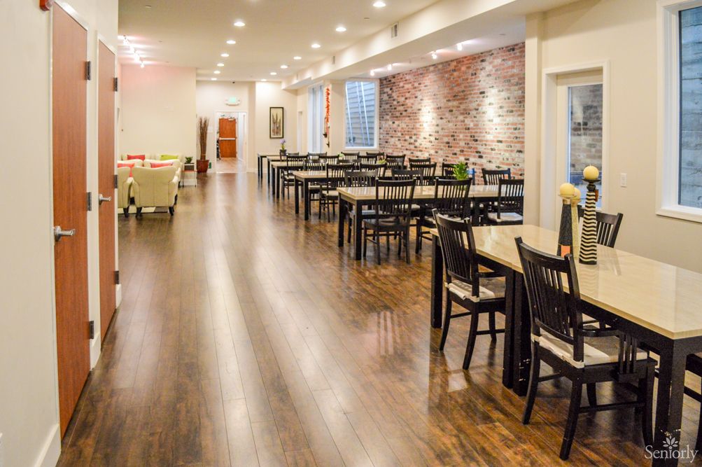 A spacious restaurant interior with neatly arranged tables and chairs, featuring a brick accent wall and wooden flooring.