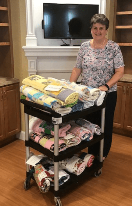 A person stands in a room next to a cart filled with quilts.