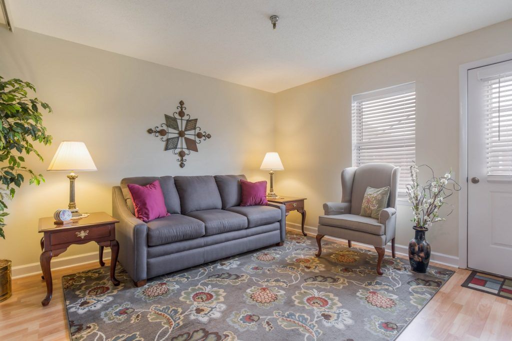 A cozy living room featuring a gray sofa with pink pillows, an armchair, and decorative elements including lamps and wall art.