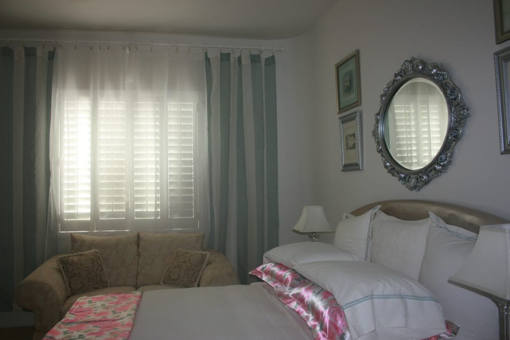 A cozy bedroom with a bed, mirror, and curtains.