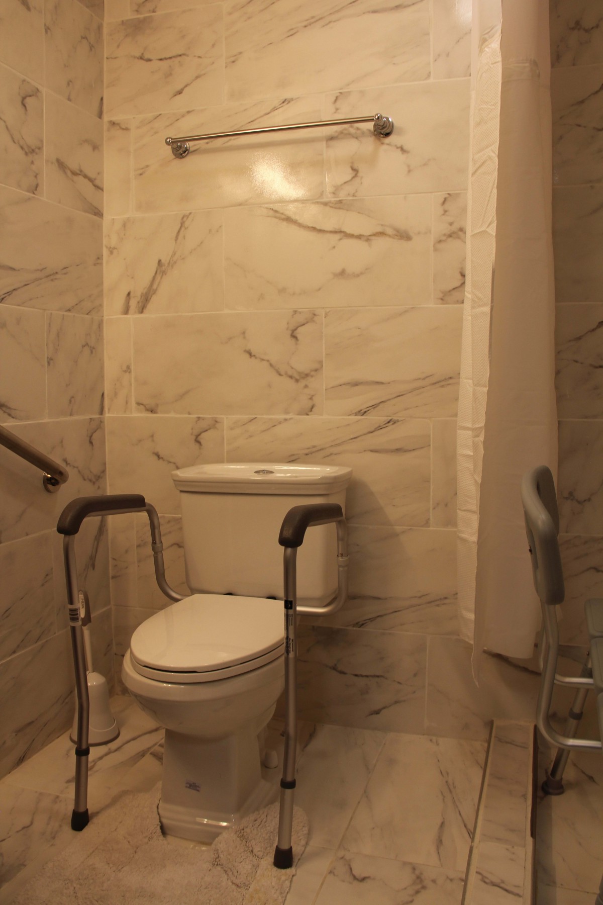 An accessible bathroom with a toilet equipped with safety rails and marble tiled walls.