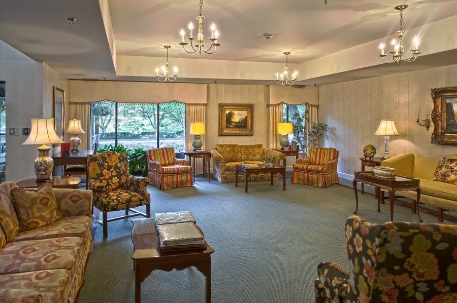 A cozy, traditionally decorated living room with multiple seating arrangements and large windows bringing in natural light.
