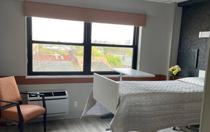 A hospital room with a single bed, large windows, and a chair.