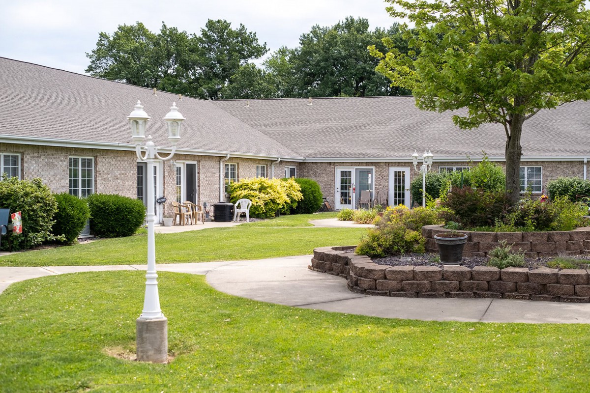 A well-maintained garden area with a building, featuring pathways, lamp posts, and lush greenery.