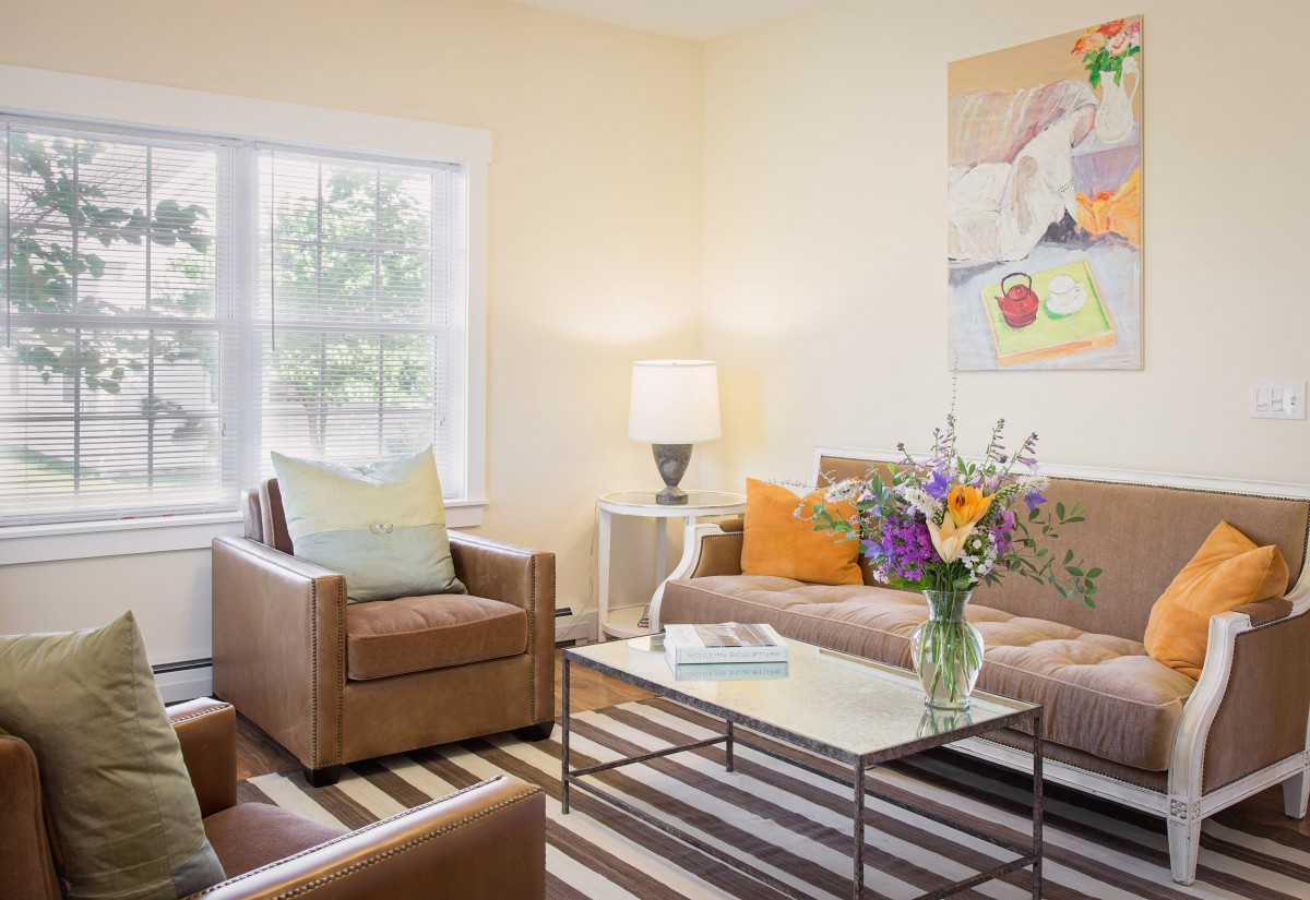 A cozy living room with modern furniture, including a sofa and two chairs, accented by colorful pillows and a bouquet of flowers on the coffee table.