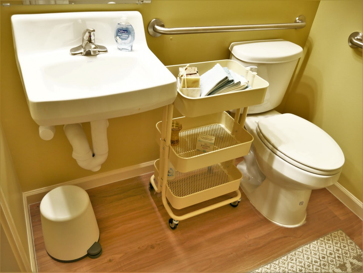 A well-organized bathroom with a sink, toilet, and a storage cart on wooden flooring.