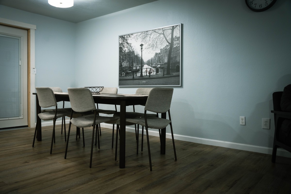 A minimalist dining room with a wooden table, chairs, and a framed artwork on the wall.