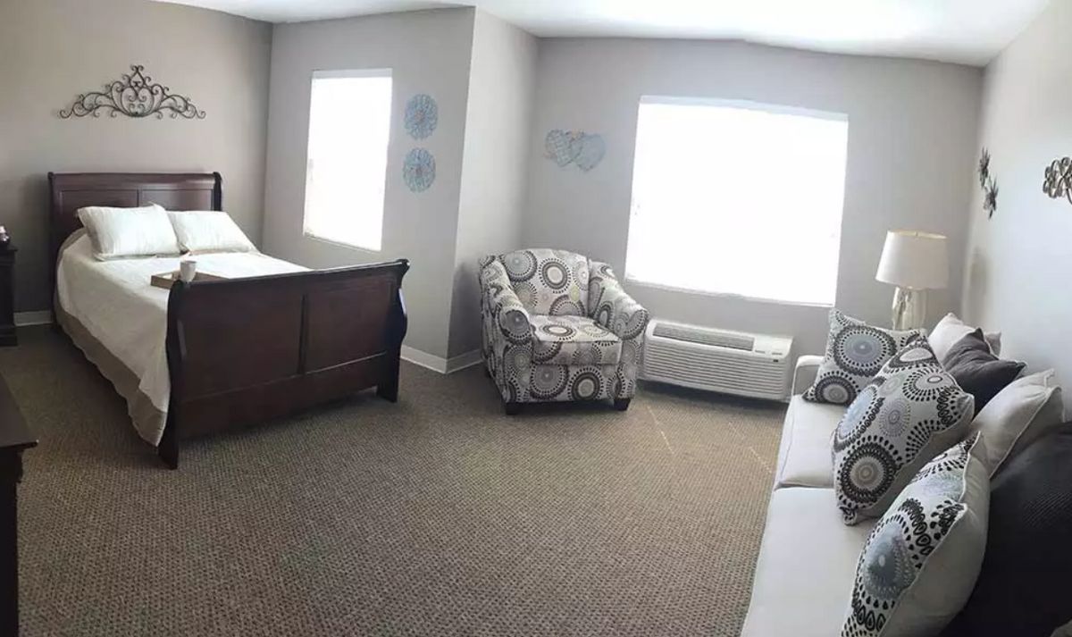 A cozy bedroom with a wooden bed, patterned armchair, and large windows letting in natural light.