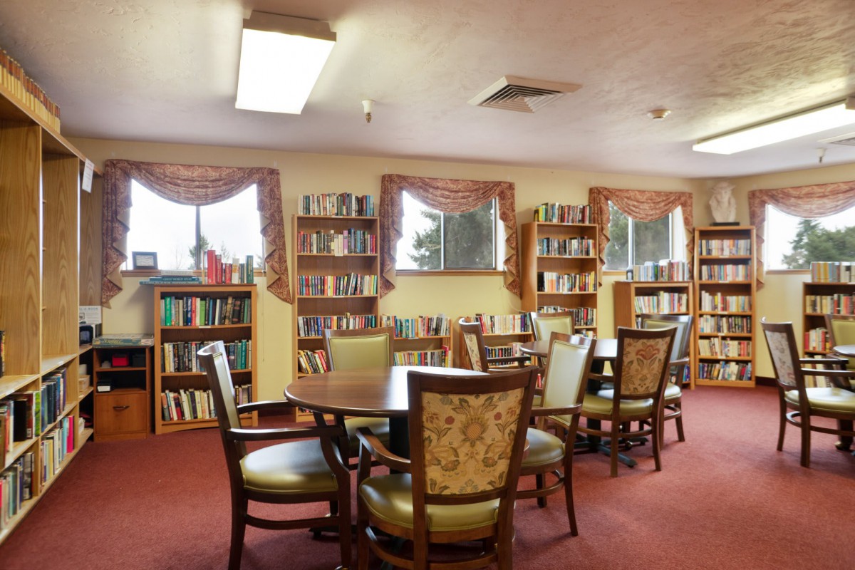 A cozy library room with bookshelves lining the walls and tables with chairs in the center.