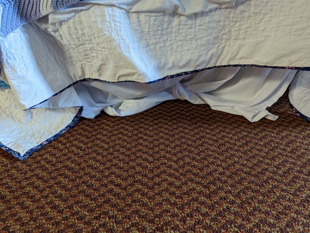 A bed with a blanket draped over it, resting on a patterned carpet.