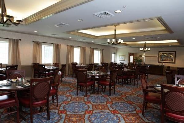 An empty dining room with neatly arranged tables and chairs, featuring elegant lighting and a patterned carpet.