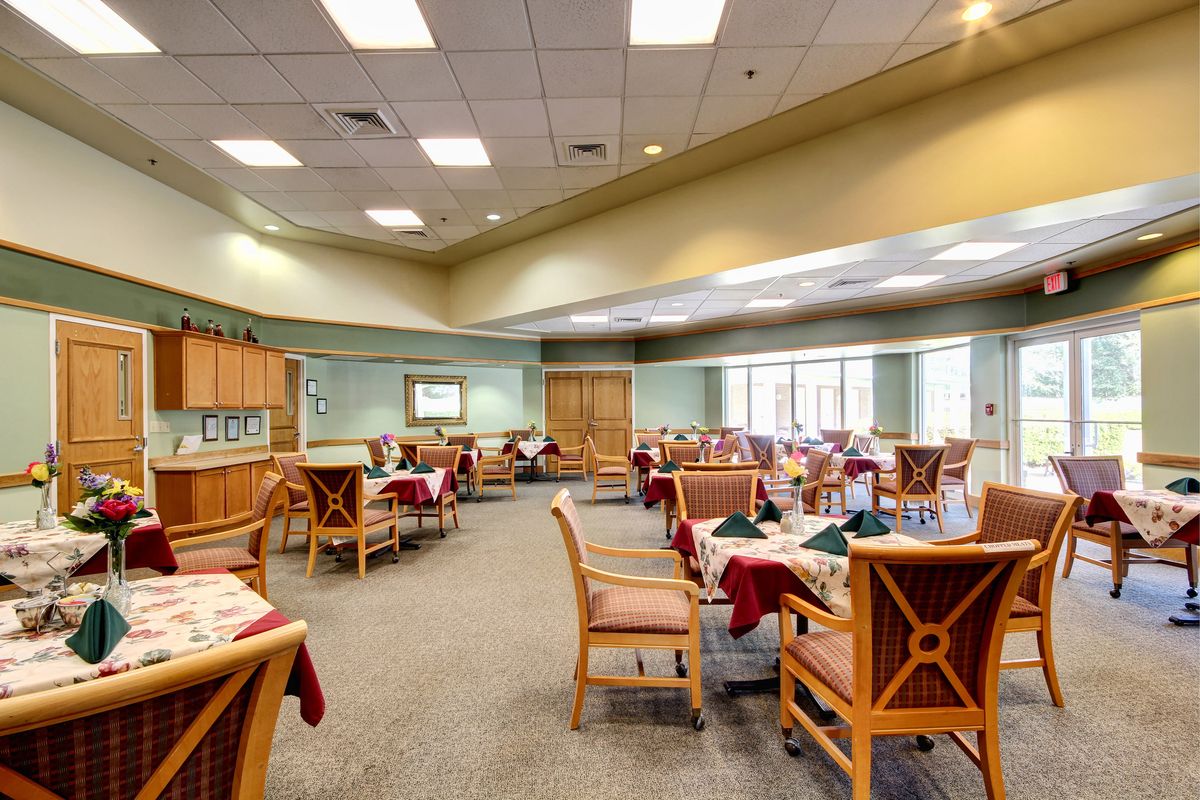 A spacious dining room with neatly arranged tables and chairs, featuring elegant table settings and bright ceiling lights.