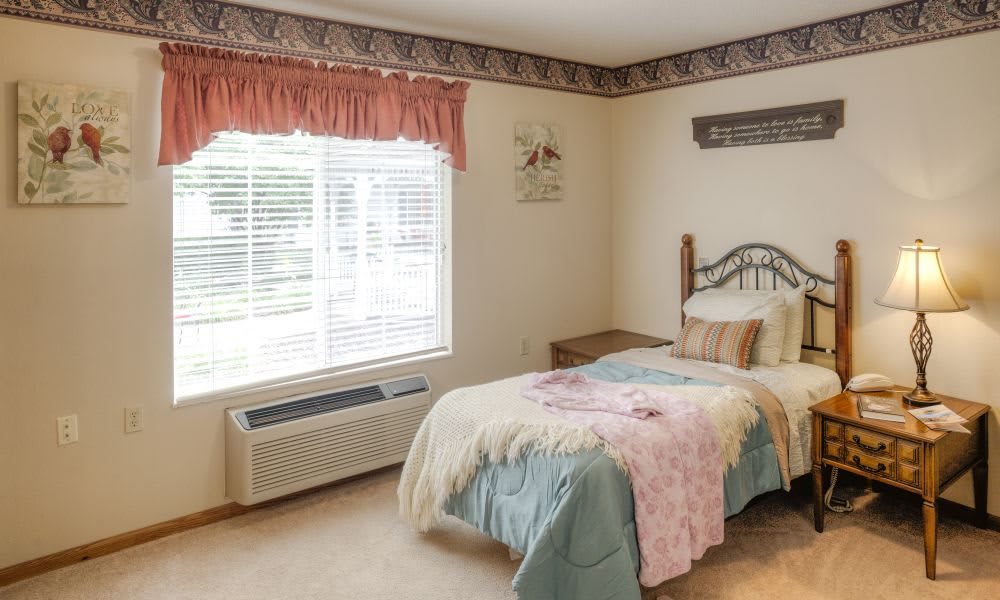 A cozy bedroom with a single bed, bedside table, and patterned trim along the ceiling.