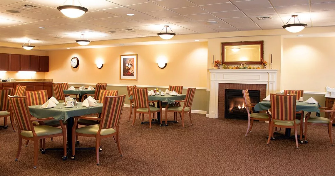 A cozy and elegant dining room with wooden tables and chairs, featuring a lit fireplace.