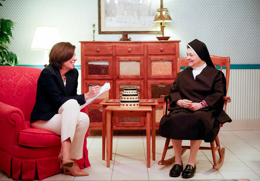 A conversation between a woman in casual attire and a nun in traditional religious dress, set in a cozy living room.