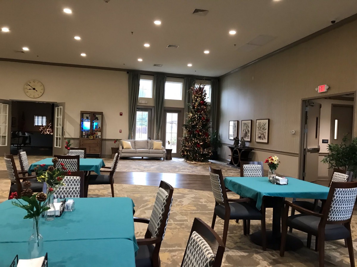 A well-decorated dining area with tables covered in teal tablecloths, featuring a large Christmas tree in the corner.