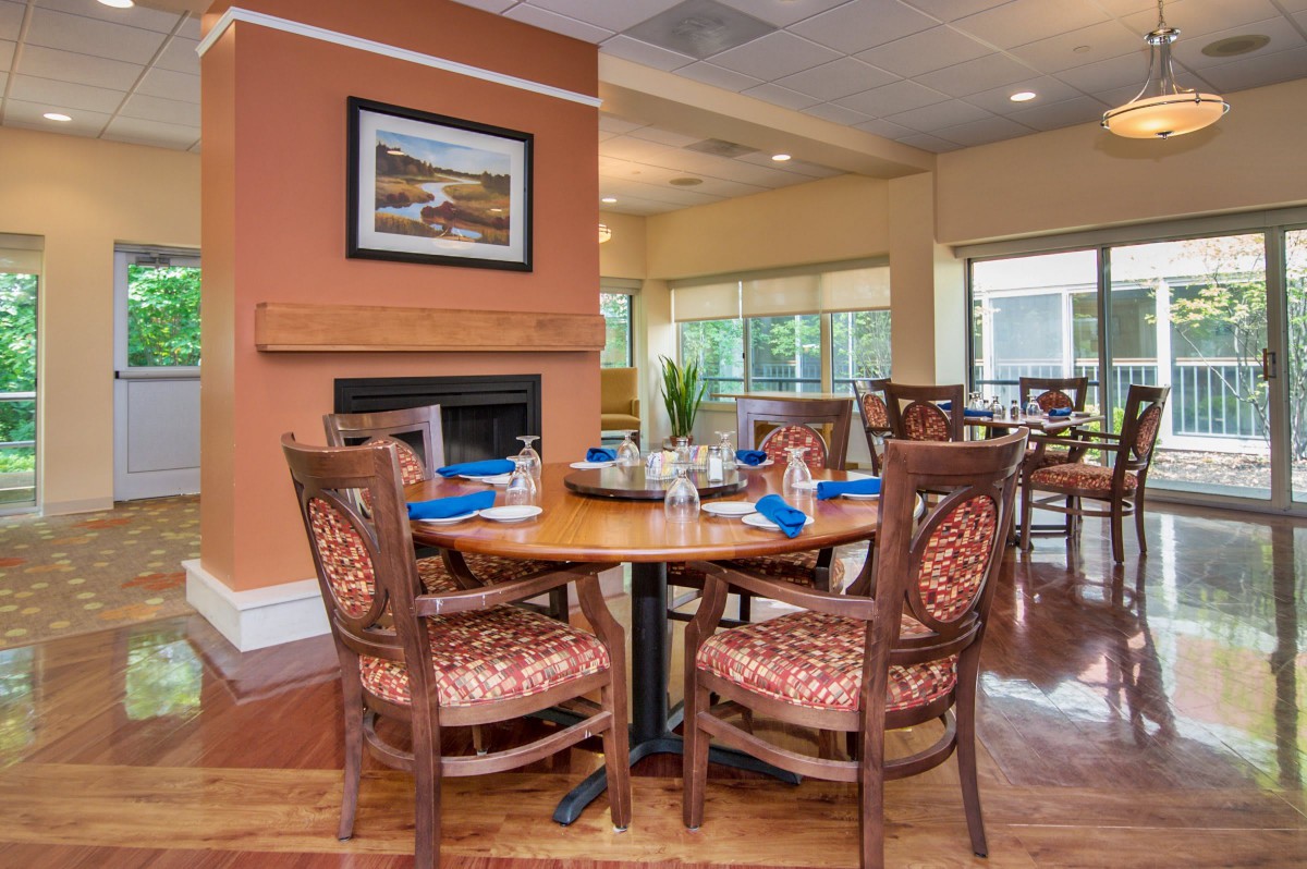 A cozy dining area with a well-set table and comfortable chairs, featuring warm interior decor and large windows.