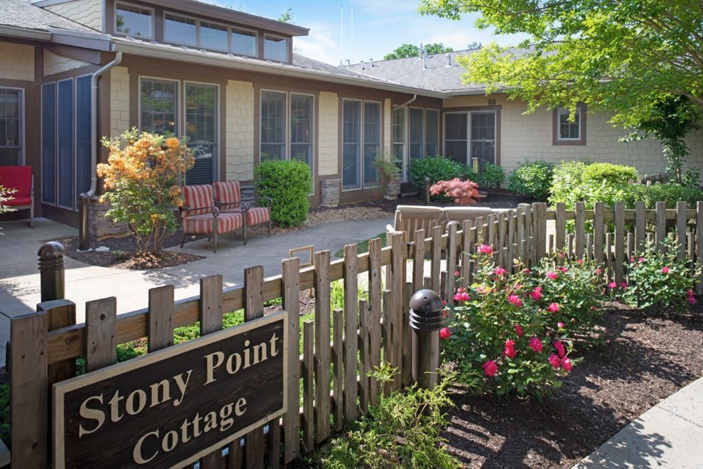 A charming cottage with a garden and wooden fence, featuring a cozy patio area with seating and vibrant flowers.