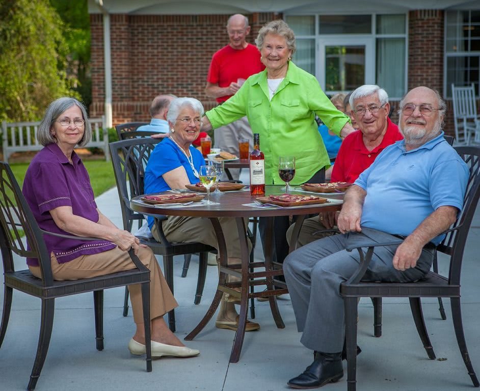 A group of seniors enjoying a gathering outdoors around a patio table.
