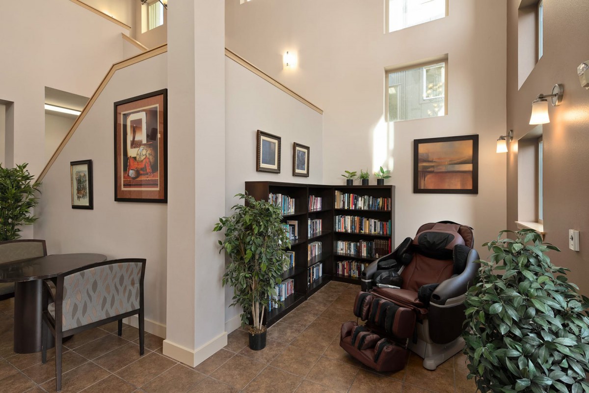 A cozy reading nook with a bookshelf, massage chair, and indoor plants.