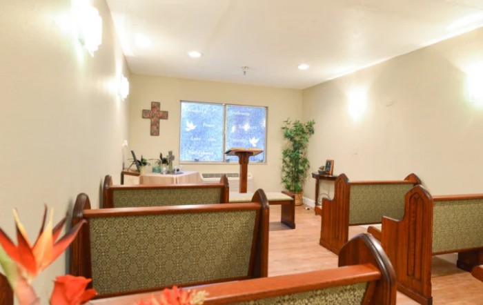 A small chapel with wooden pews, an altar, and a cross on the wall.