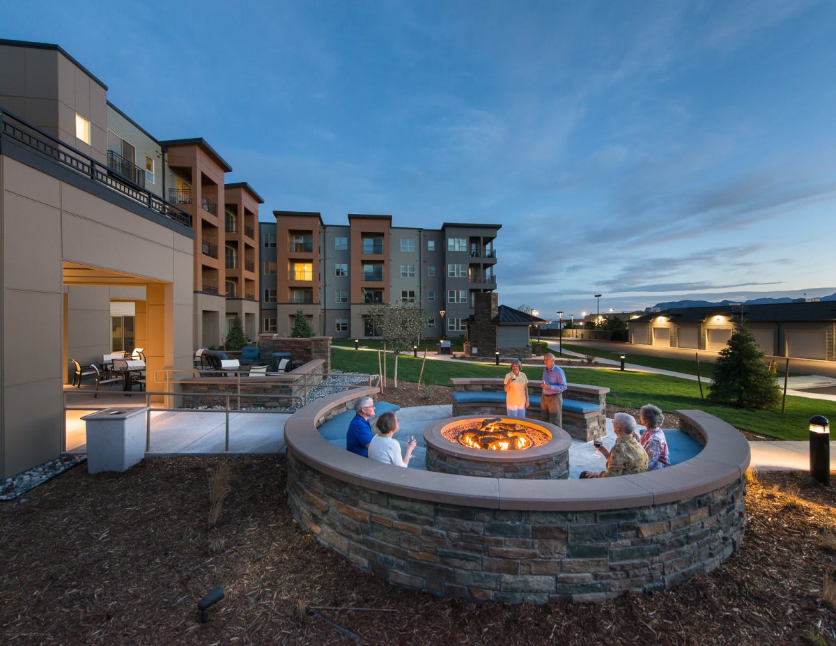 Residents gather around a fire pit in the courtyard of a modern apartment complex during the evening.
