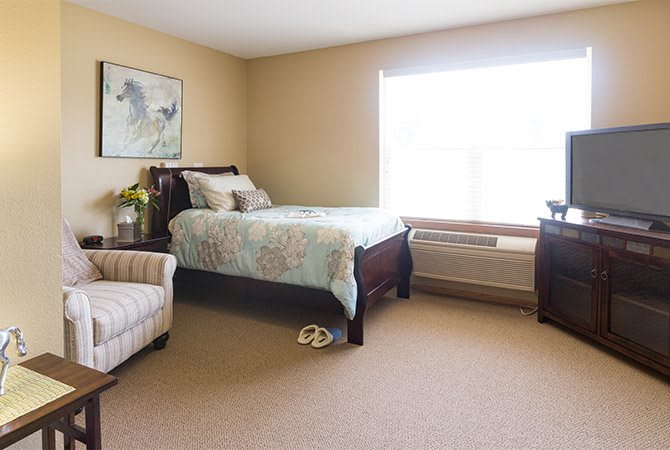 A cozy bedroom with a bed, armchair, and a large window providing natural light.