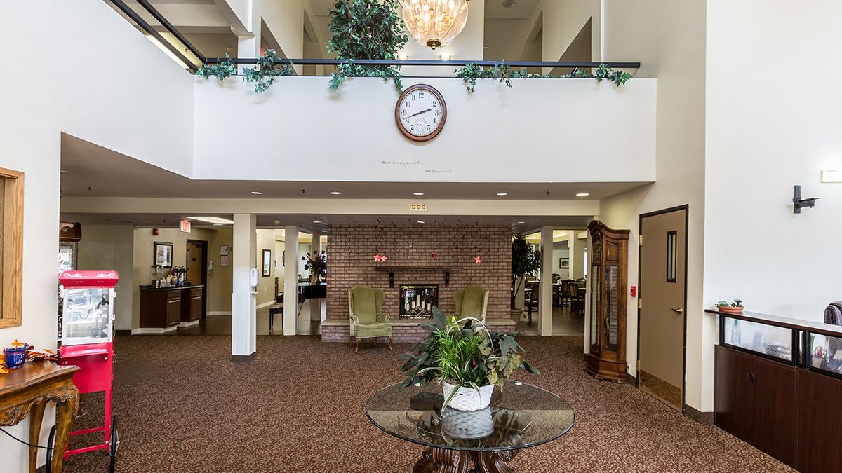 A spacious lobby featuring a central clock, chandelier, and seating area surrounded by plants.
