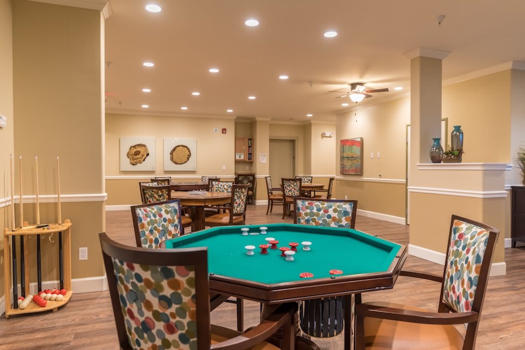 A spacious game room featuring a poker table with cards and chips, surrounded by comfortable chairs and warmly lit interior.