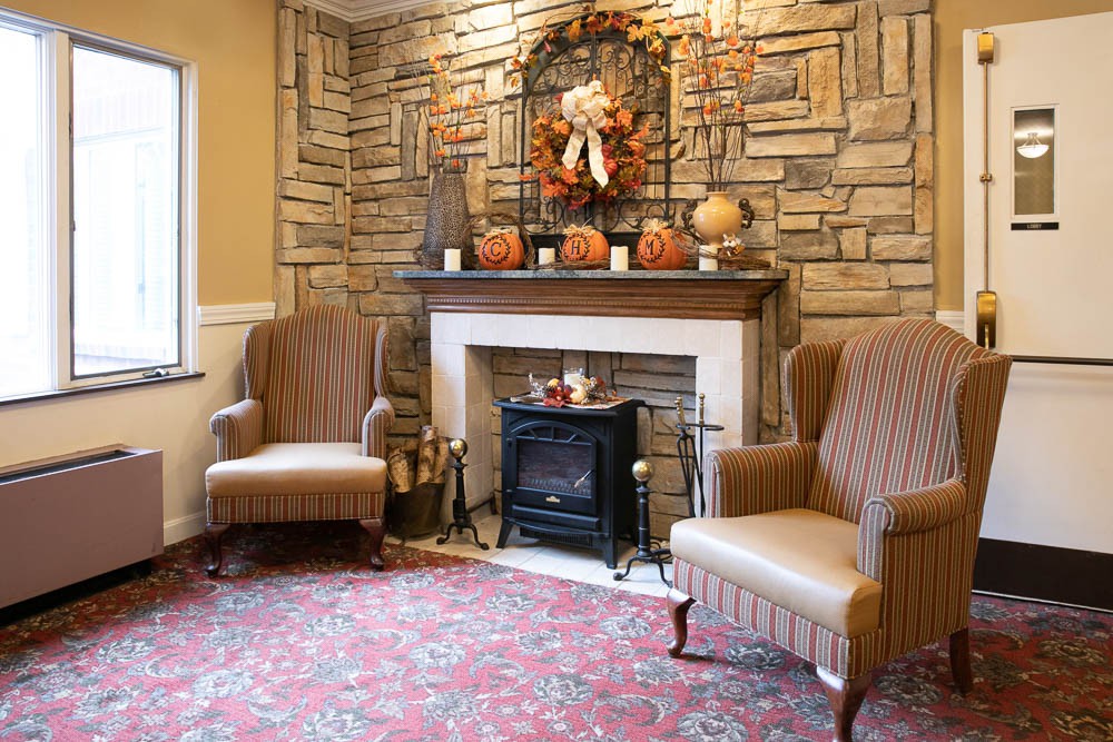 A cozy living room with a stone fireplace, decorated with autumn-themed ornaments and two armchairs.