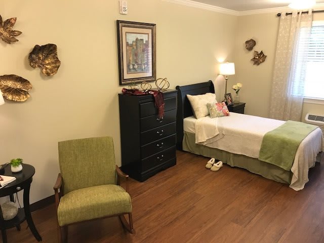 A cozy bedroom with a single bed, green chair, and wooden flooring.