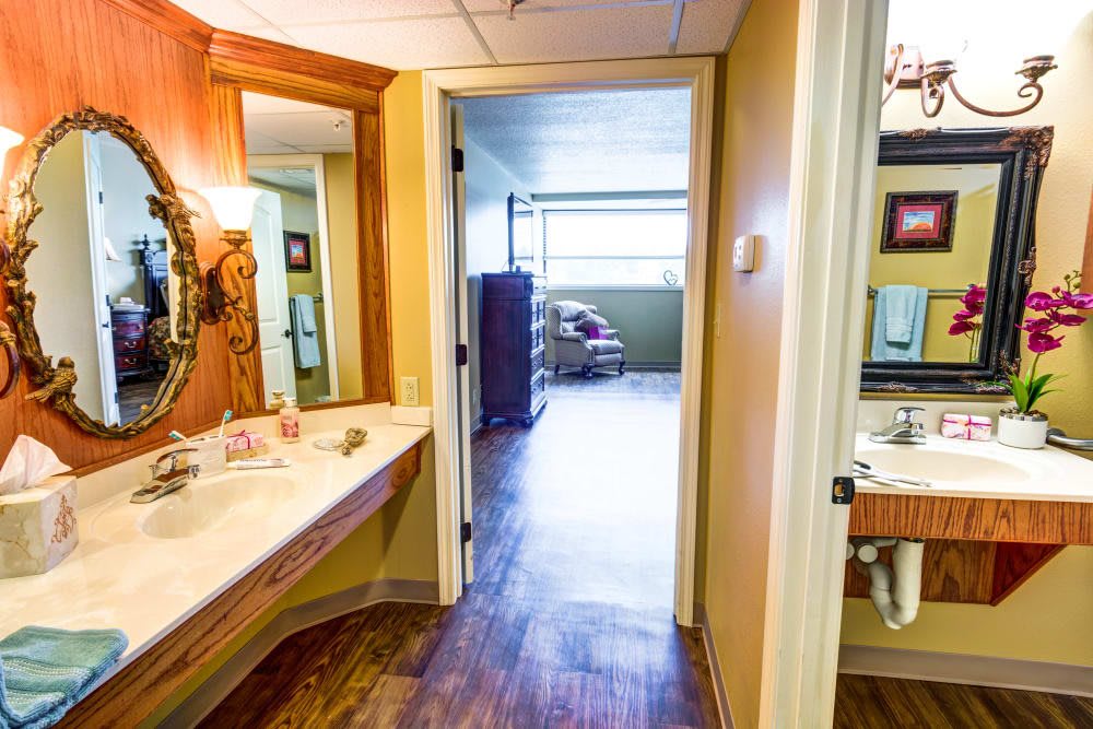 A bathroom with a sink and mirror, leading into a hallway with hardwood flooring.