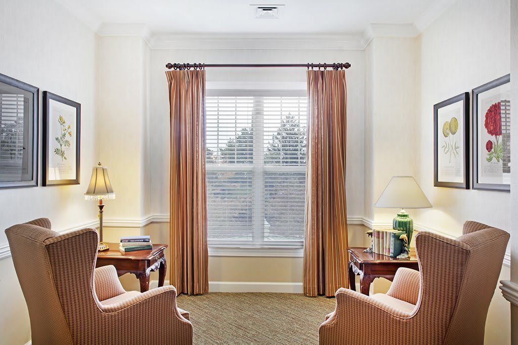 A cozy living room interior with two chairs facing a window, flanked by lamps and tables.