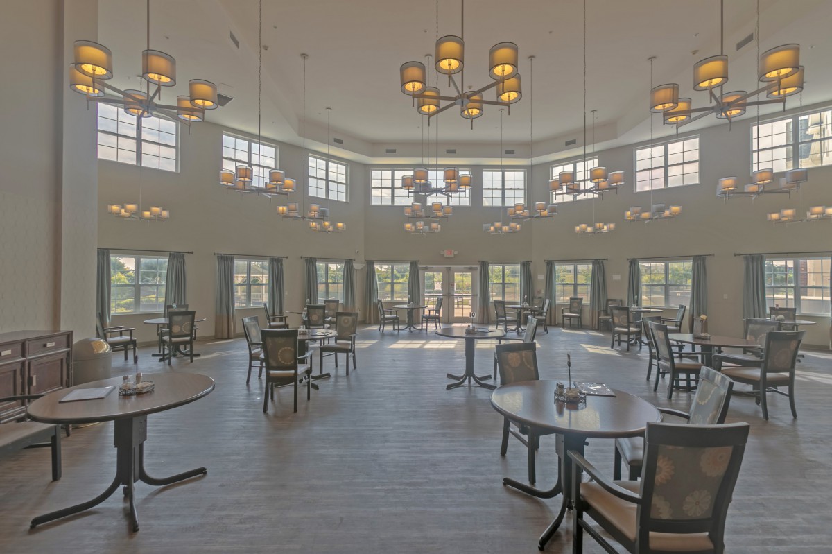 An empty dining room with tables, chairs, and large windows under decorative chandeliers.