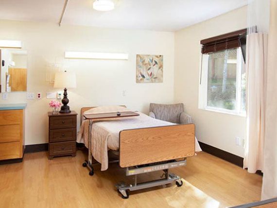 A clean and well-lit hospital room with a single bed, side table, and window.