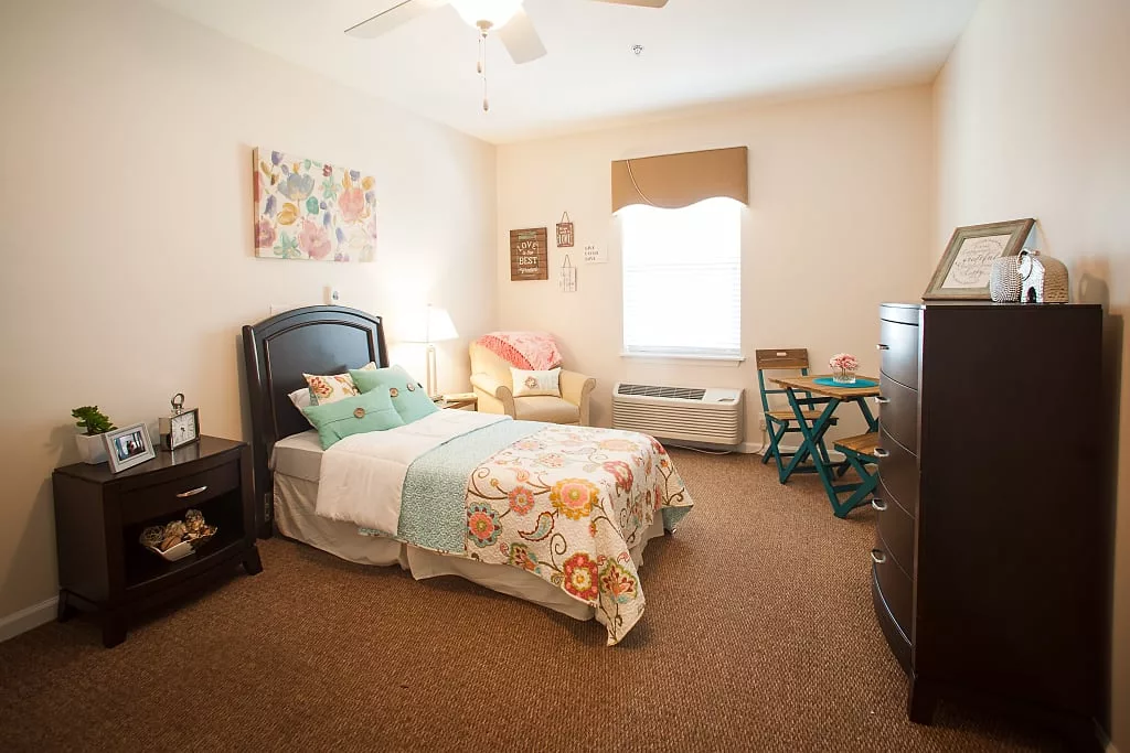 A cozy bedroom with a single bed featuring colorful bedding, a comfortable chair, and a small table near the window.