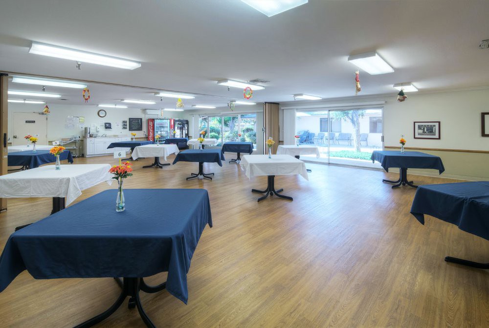 A spacious dining area with neatly arranged tables and chairs, decorated with tablecloths and flowers.